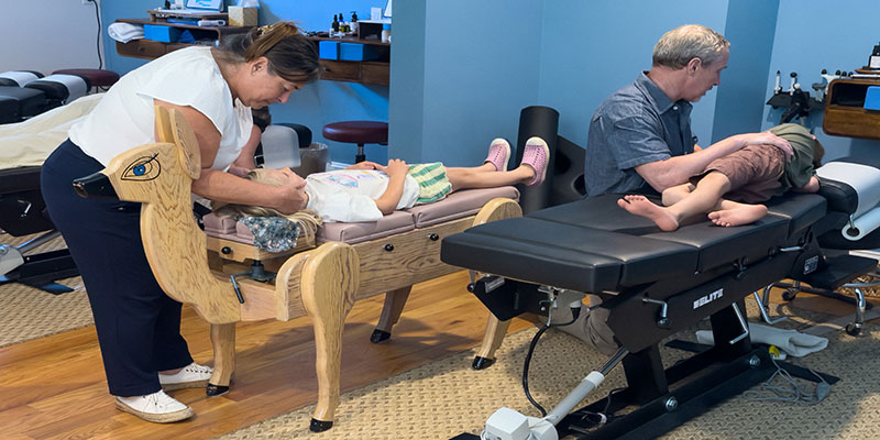 Dr Emily Bobson and Dr Noel Plasker treating children on chiropractic tables at Hudson Valley Chiropractic.